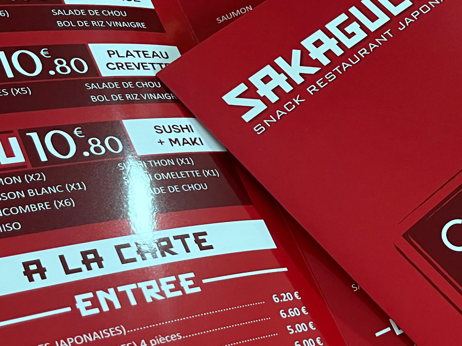 Gros plan sur les cartes de menu Sakaguchi montrant les reflets du pelliculage brillant et le bord du support.