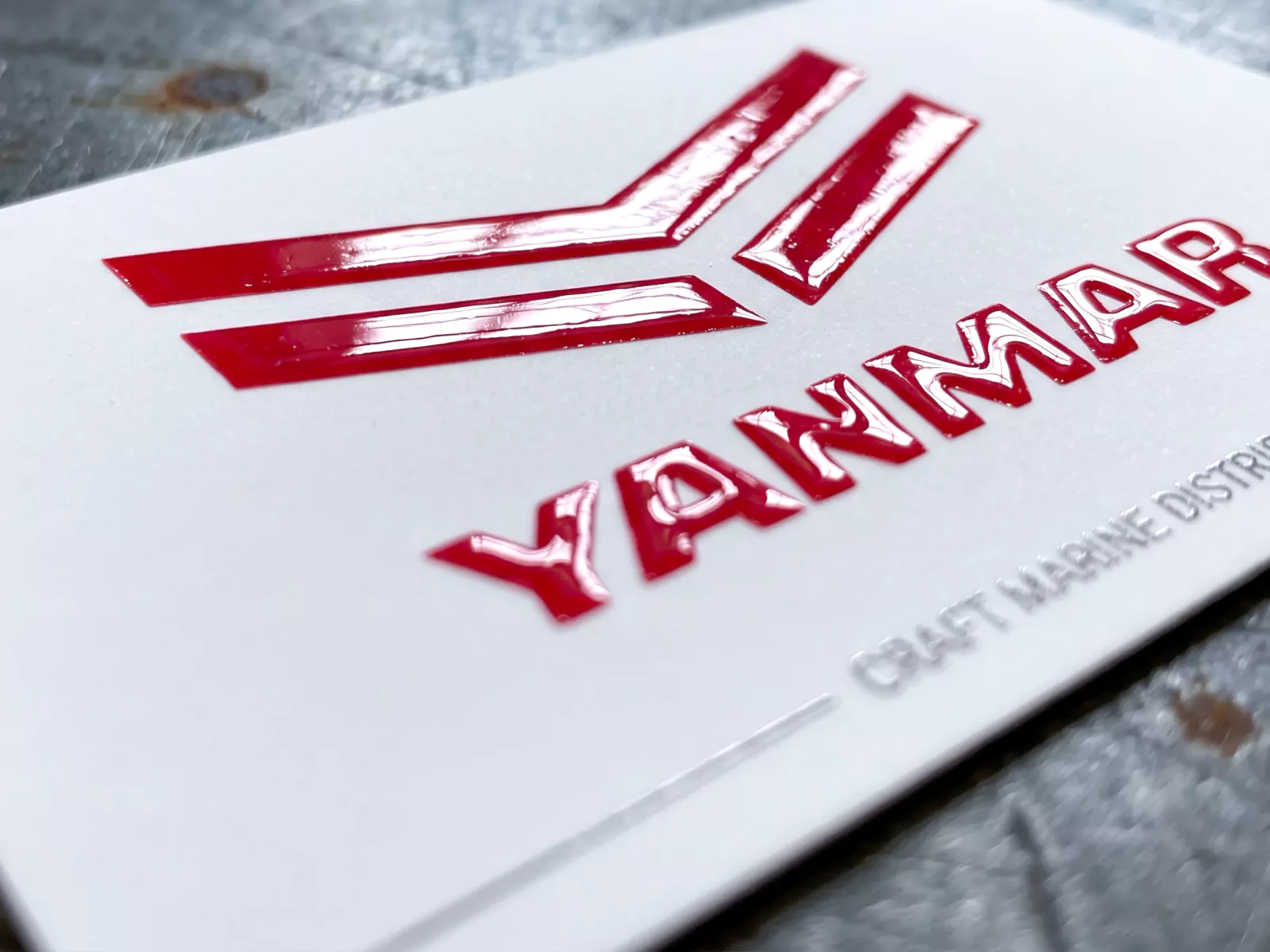 Gros plan sur le relief brillant du Gel 3D appliqué au logo Yanmar rouge sur une carte de visite.
