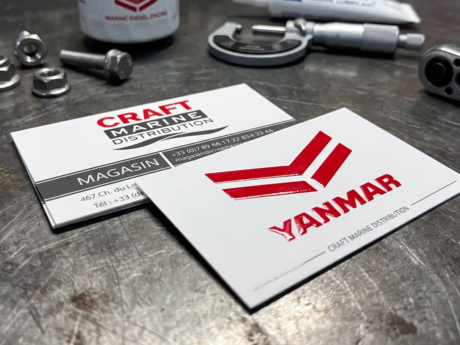 Cartes de visite Craft Marine Distribution avec logo Yanmar rouge en Gel 3D, présentées sur un établi.