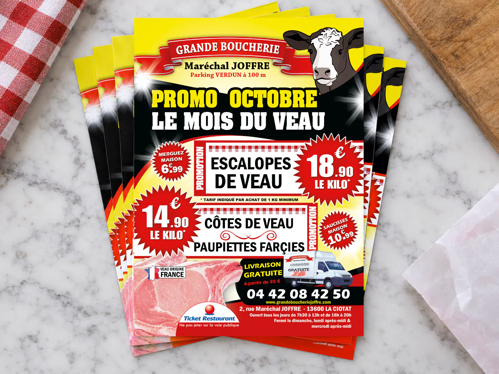 Flyers A5 « Le mois du veau » de la Grande Boucherie Maréchal Joffre posés en éventail sur un comptoir en marbre.