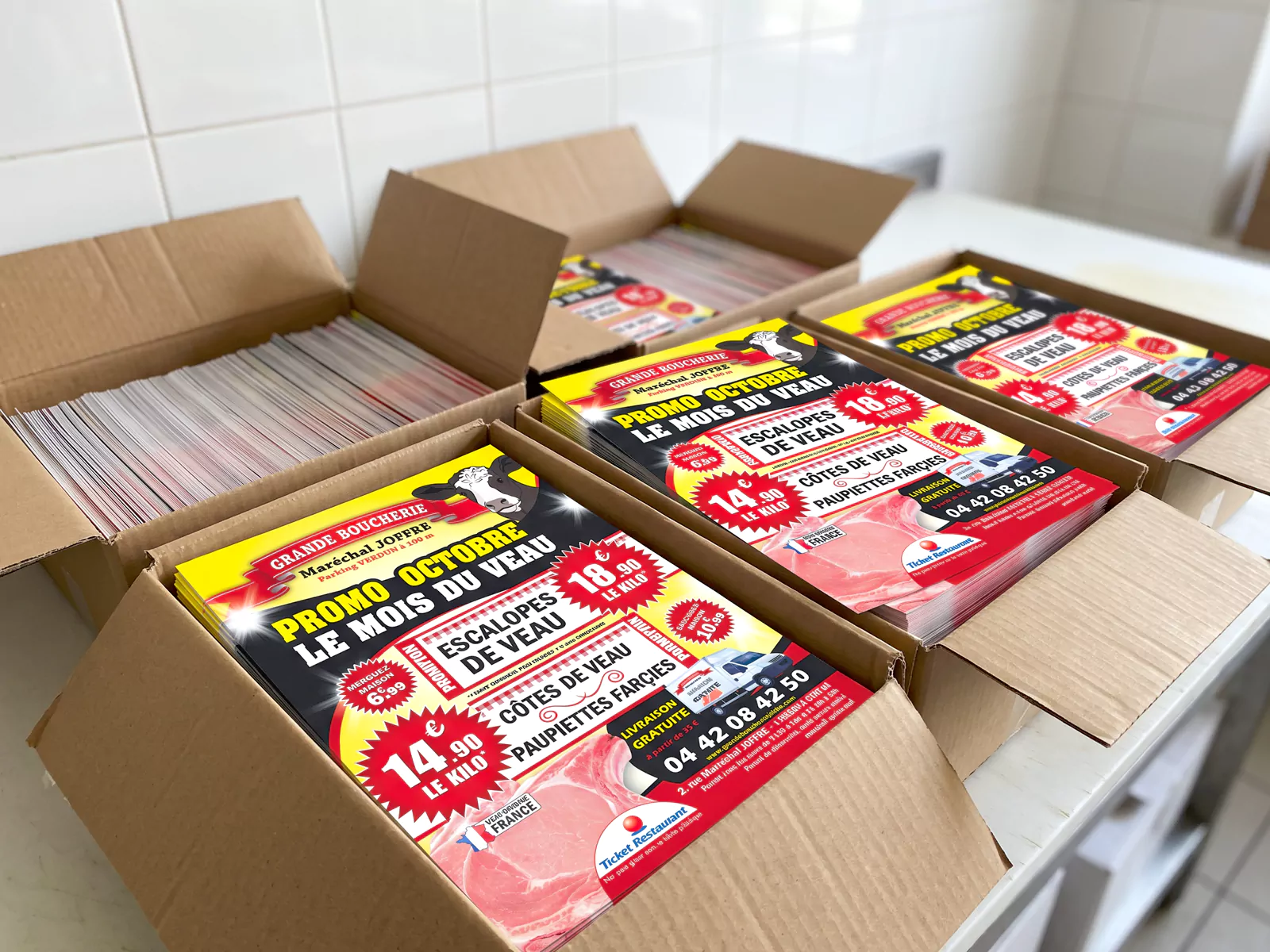 Cartons ouverts remplis de flyers A5 « Le mois du veau » de la Grande Boucherie Maréchal Joffre.